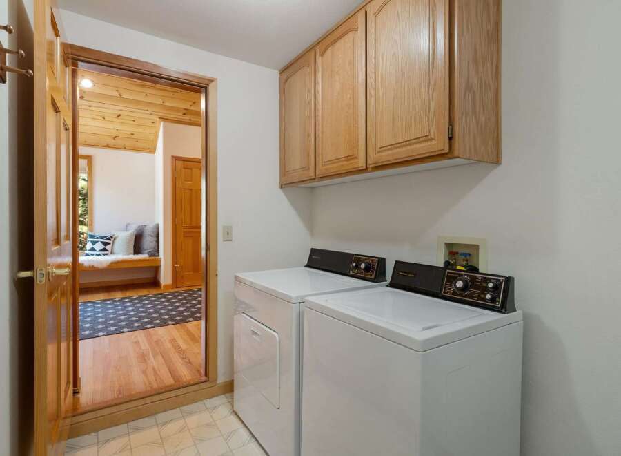 This laundry room features a white top-load washer and dryer set, complemented by light wood cabinetry above for ample storage.