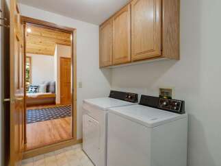This laundry room features a white top-load washer and dryer set, complemented by light wood cabinetry above for ample storage.