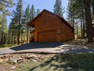Nestled amidst tall pine trees, this charming wooden cabin features a spacious two-car garage with a beautiful wood-paneled door and decorative glass windows.