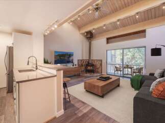 Experience modern living in this stunning open-concept space, featuring a sleek kitchen island and a cozy living area centered around a stone-clad fireplace.