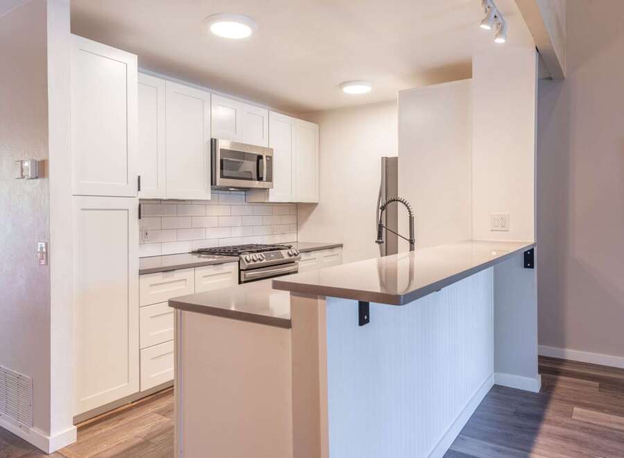 This modern kitchen features sleek white cabinetry, a stainless steel gas range, and a microwave.