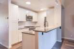 This modern kitchen features sleek white cabinetry, a stainless steel gas range, and a microwave.
