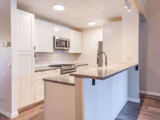 This modern kitchen features sleek white cabinetry, a stainless steel gas range, and a microwave.