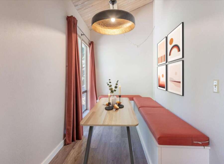 Enjoy cozy meals in this charming dining nook featuring a light wood table and built-in bench seating with vibrant coral cushions.