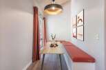 Enjoy cozy meals in this charming dining nook featuring a light wood table and built-in bench seating with vibrant coral cushions.
