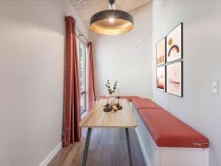 Enjoy cozy meals in this charming dining nook featuring a light wood table and built-in bench seating with vibrant coral cushions.