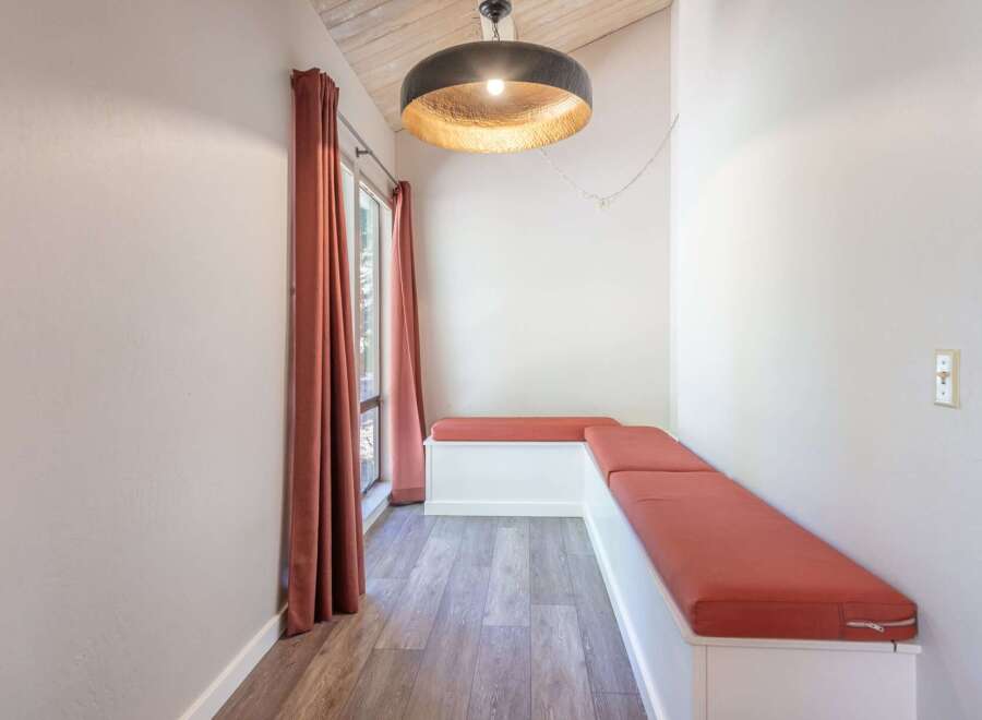 Enjoy cozy meals in this charming dining nook featuring a light wood table and built-in bench seating with vibrant coral cushions.