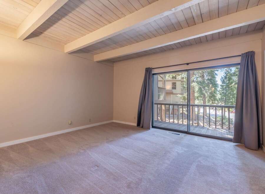 Step into this inviting room featuring a vaulted wood-beamed ceiling and plush carpeting, creating a warm and airy atmosphere.