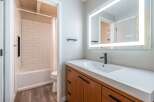 This modern bathroom features a sleek vanity with a white countertop and a black faucet, complemented by a large, illuminated mirror.