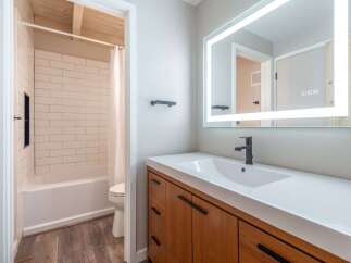 This modern bathroom features a sleek vanity with a white countertop and a black faucet, complemented by a large, illuminated mirror.