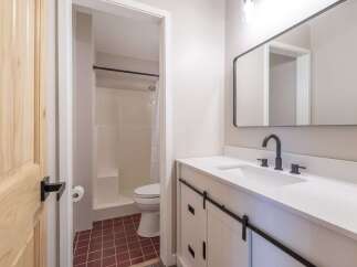 This modern bathroom features a sleek white vanity with barn-style doors and a black faucet, complemented by a large rectangular mirror.
