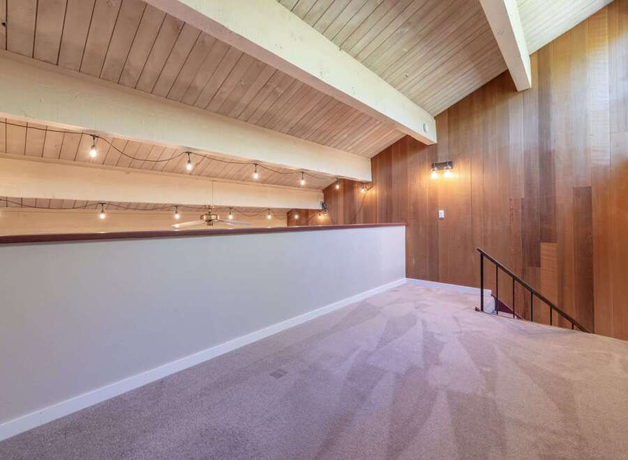 Experience the unique charm of this loft space, featuring a vaulted wood-paneled ceiling with exposed beams and decorative string lights.