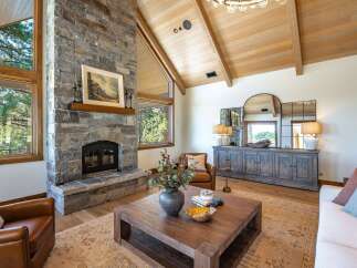 Experience rustic elegance in this stunning living room, featuring a grand stone fireplace and vaulted wood-beamed ceilings.