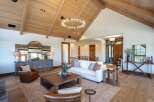 Experience luxury living in this stunning great room, featuring a vaulted wood-beamed ceiling and a modern circular chandelier.