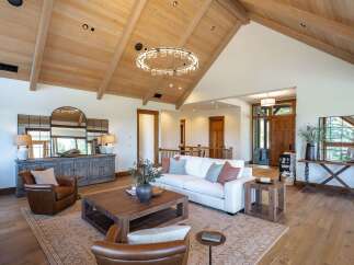 Experience luxury living in this stunning great room, featuring a vaulted wood-beamed ceiling and a modern circular chandelier.