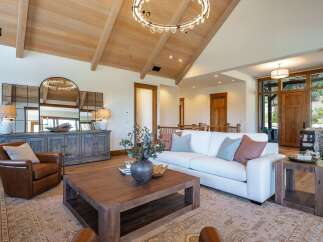 Experience luxurious living in this stunning great room, featuring a vaulted wood-beamed ceiling and a modern circular chandelier.