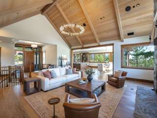 Experience luxurious mountain living in this stunning great room, featuring a vaulted wood-beamed ceiling and a modern circular chandelier.