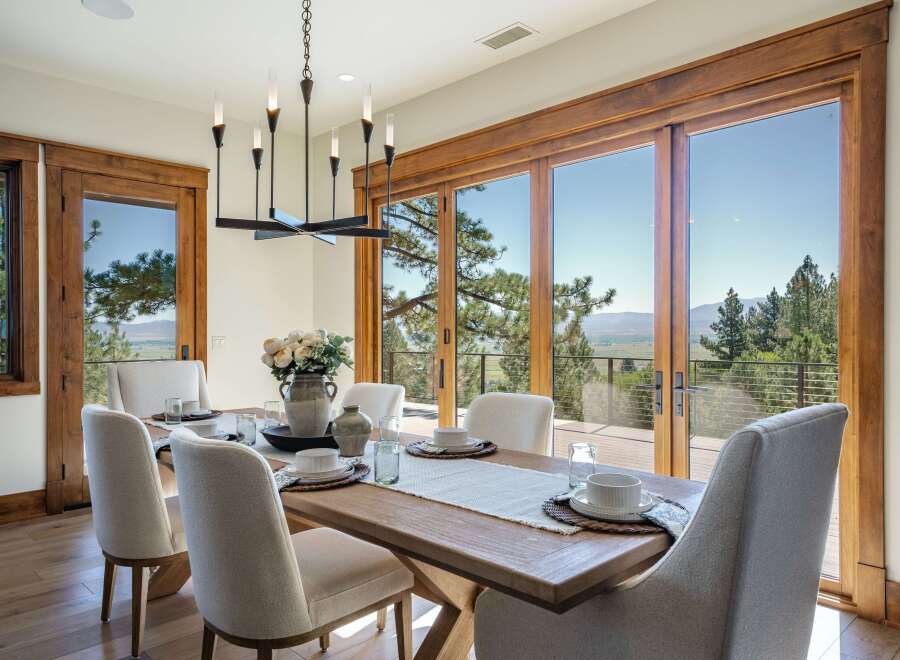 Experience breathtaking mountain views from this elegant dining room, featuring a large wooden table set for six and a modern chandelier.