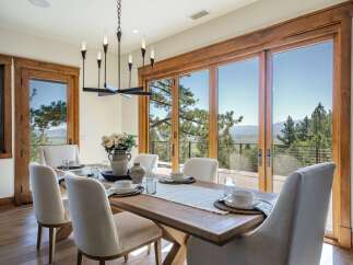 Experience breathtaking mountain views from this elegant dining room, featuring a large wooden table set for six and a modern chandelier.