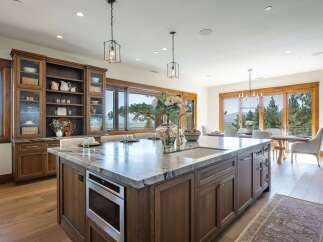 Experience luxury living in this stunning kitchen featuring a large marble island with a built-in microwave and sink, complemented by custom wood cabinetry.