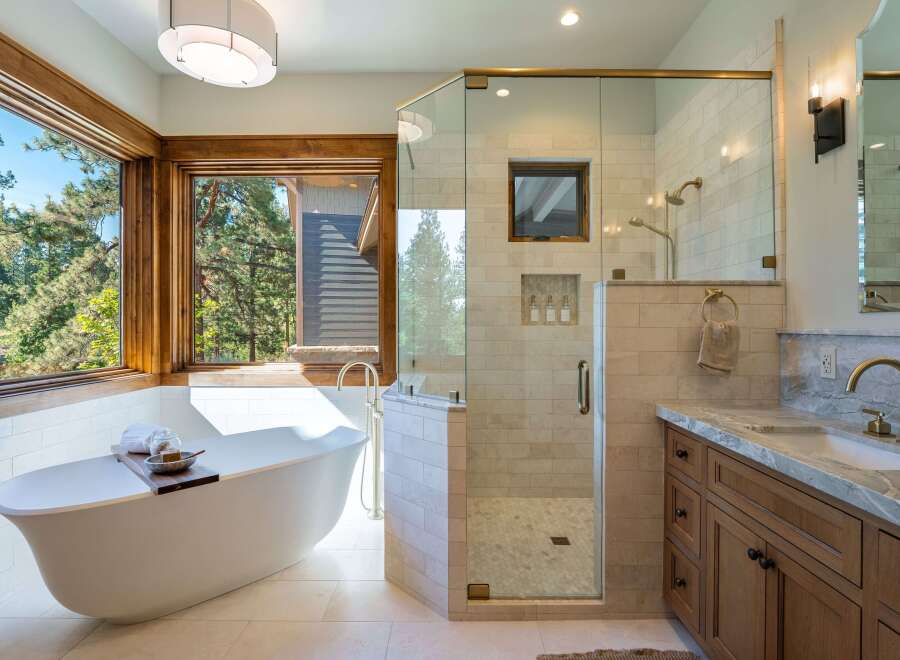 Experience luxury in this stunning bathroom featuring a freestanding soaking tub with a picturesque view of the surrounding forest.
