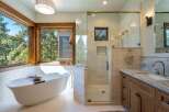 Experience luxury in this stunning bathroom featuring a freestanding soaking tub with a picturesque view of the surrounding forest.
