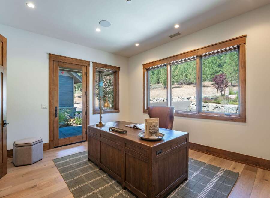 This home office features a large wooden desk with a leather chair, complemented by a stylish plaid rug and a comfortable ottoman.