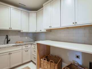 Discover this beautifully appointed laundry room featuring pristine white cabinetry and elegant subway tile backsplash.