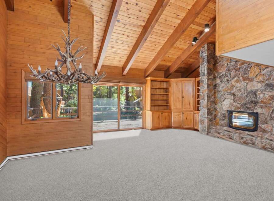 Experience rustic charm in this spacious living area featuring a stunning antler chandelier and a grand stone fireplace.