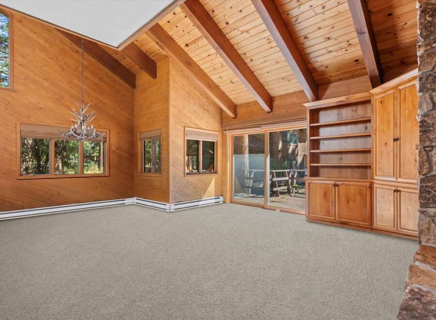 Experience rustic charm in this spacious living area featuring a vaulted wood-paneled ceiling with exposed beams and a unique antler chandelier.
