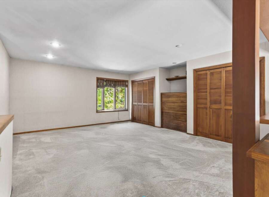This spacious room features plush carpeting and ample natural light from a large window overlooking lush greenery.