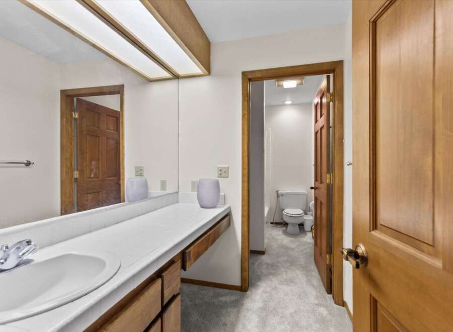 This bathroom features a spacious vanity with a white tiled countertop and a large mirror, perfect for your morning routine.