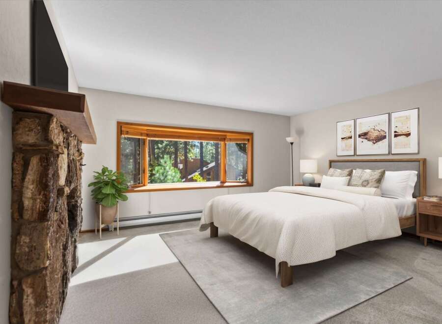 Experience cozy living in this charming bedroom, featuring a rustic stone fireplace and a large bay window that floods the space with natural light and offers picturesque forest views.