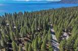 Experience the ultimate lakeside living with this stunning aerial view of homes nestled among tall pine trees, offering breathtaking vistas of a vast, blue lake and distant mountains.