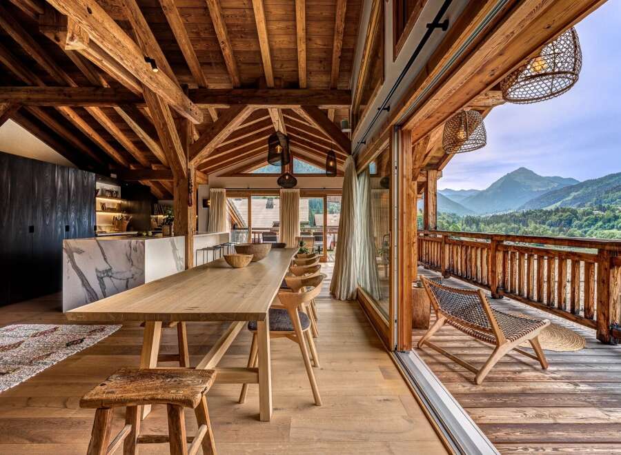 Experience luxurious mountain living in this stunning chalet, featuring a spacious open-plan dining and kitchen area with a marble island and a large wooden dining table.