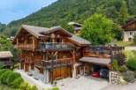 Experience luxury mountain living in this stunning wooden chalet, nestled against a lush green hillside.