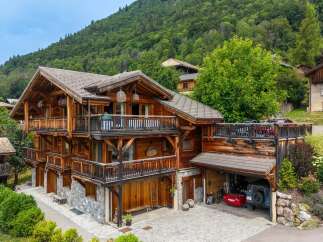 Experience luxury mountain living in this stunning wooden chalet, nestled against a lush green hillside.