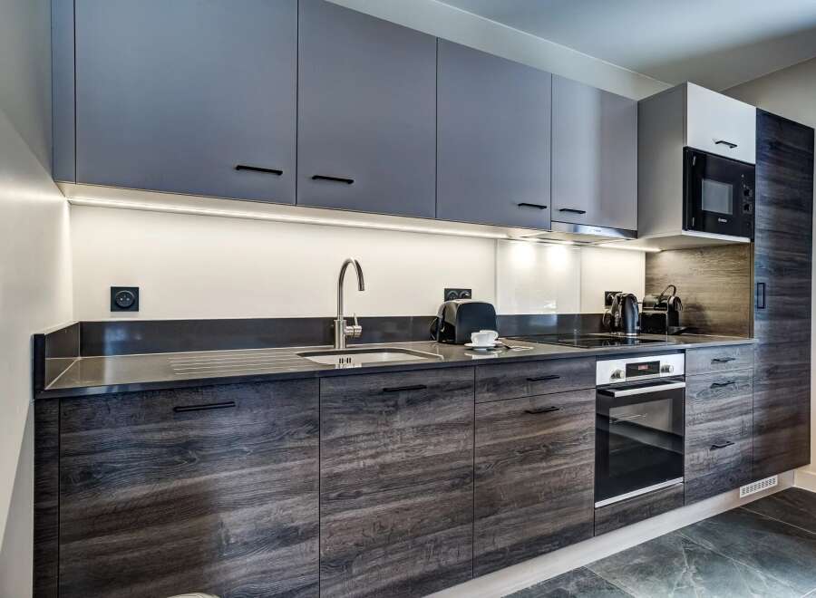 Discover this modern kitchen featuring sleek, dark wood cabinetry and contrasting grey upper cabinets.
