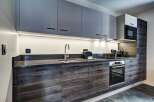 Discover this modern kitchen featuring sleek, dark wood cabinetry and contrasting grey upper cabinets.