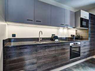 Discover this modern kitchen featuring sleek, dark wood cabinetry and contrasting grey upper cabinets.