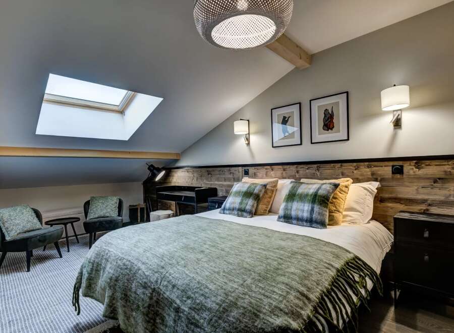 Experience cozy living in this charming attic bedroom, featuring a comfortable bed adorned with plaid pillows and a plush green throw.