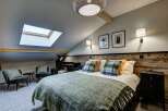 Experience cozy living in this charming attic bedroom, featuring a comfortable bed adorned with plaid pillows and a plush green throw.