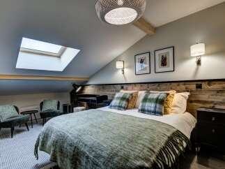 Experience cozy living in this charming attic bedroom, featuring a comfortable bed adorned with plaid pillows and a plush green throw.