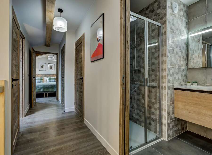 Discover this charming hallway featuring rustic wooden doors and a modern bathroom with a sleek shower and vanity.