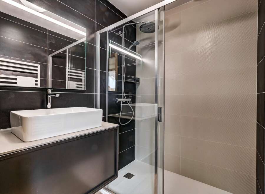 Experience modern luxury in this stunning bathroom featuring a sleek vessel sink atop a dark vanity, complemented by a spacious glass-enclosed shower with a rainfall showerhead.
