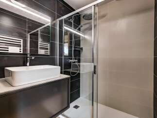 Experience modern luxury in this stunning bathroom featuring a sleek vessel sink atop a dark vanity, complemented by a spacious glass-enclosed shower with a rainfall showerhead.