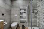 This modern bathroom features a sleek toilet, a stylish heated towel rack, and a spacious glass-enclosed shower with attractive hexagonal tile accents.