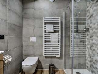 This modern bathroom features a sleek toilet, a stylish heated towel rack, and a spacious glass-enclosed shower with attractive hexagonal tile accents.