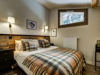 Experience cozy mountain living in this charming bedroom, featuring a rustic wooden headboard and a plush plaid blanket perfect for chilly evenings.