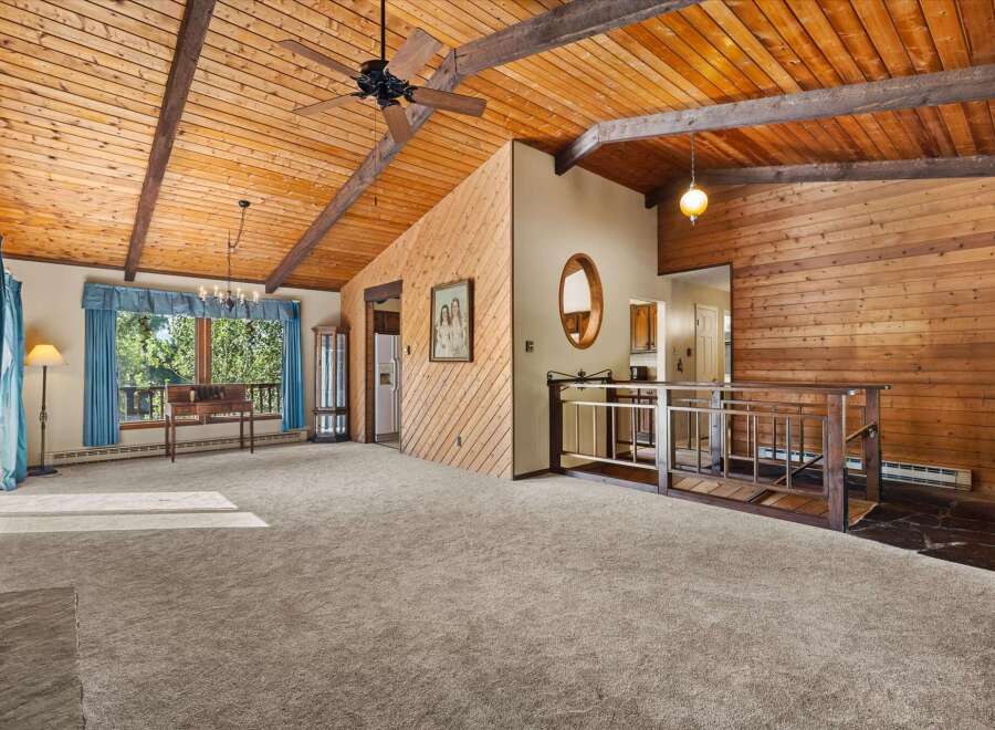 Experience rustic charm in this spacious living area featuring a vaulted wood-paneled ceiling with exposed beams and a ceiling fan.
